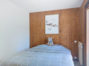 A bedroom with a wooden paneled wall, a bed with a blue quilt, and a framed picture above the bed. - Le Nerey 2 by Interhome (Saint Gervais)