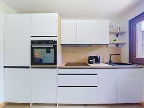 A compact kitchen with white cabinets, a built-in oven, a coffee maker, and a window. - Le Nerey 2 by Interhome (Saint Gervais)
