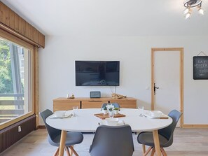 A dining area with a round table, chairs, a TV mounted on the wall, and a wooden cabinet. - Le Nerey 2 by Interhome (Saint Gervais)