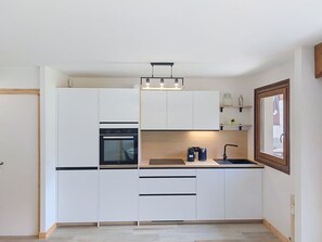 A modern kitchen with white cabinetry, a built-in oven, a sink, and a window. - Le Nerey 2 by Interhome (Saint Gervais)