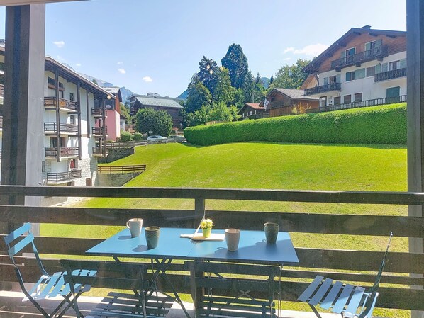 Eine Terrasse mit Tisch und Stühlen, die auf einen gepflegten Rasen und eine Reihe von Gebäuden blickt.