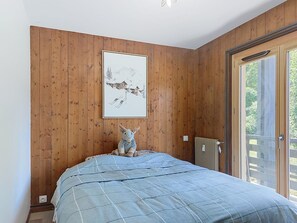 A bedroom with a bed, a wooden wall, a framed picture, a radiator, and a sliding glass door. - Le Nerey 2 by Interhome (Saint Gervais)