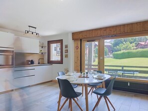 A modern kitchen with white cabinets, a built-in oven, and a dining area with a round table and four chairs. - Le Nerey 2 by Interhome (Saint Gervais)