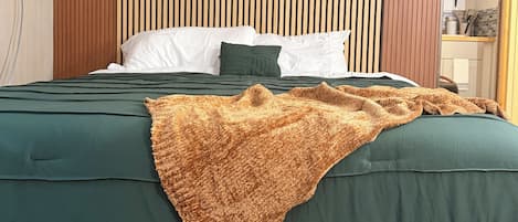 Une chambre d’hôtel avec un lit, une tête de lit en lattes de bois, une moquette à motifs et une prise de courant visible.