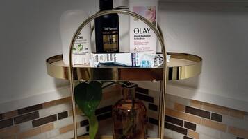 Ein Badezimmer-Waschtisch mit einem goldfarbenen Spiegelrahmen, einer Dove Body Lotion Flasche, einer Olay Feuchtigkeitscreme Flasche und einer Tressemé Körperöl Flasche.