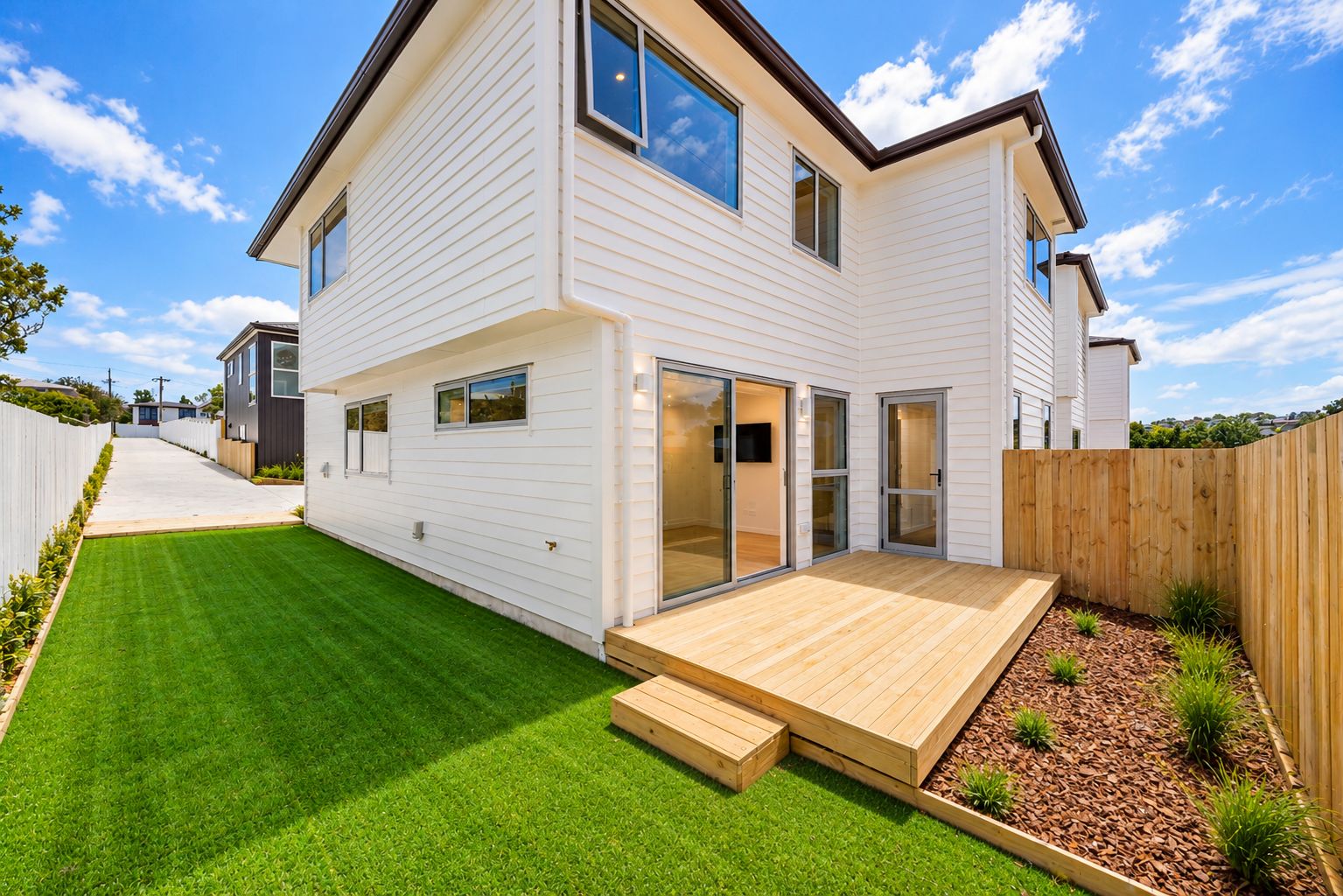 A two-story house with a well-maintained lawn, a wooden deck, and a sliding glass door leading to a patio area.
