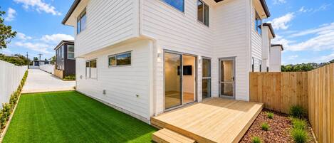 A two-story house with a well-maintained lawn, a wooden deck, and a sliding glass door leading to a patio area.