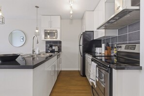 Een moderne keuken met een magnetron, fornuis, koelkast en een houten vloer.