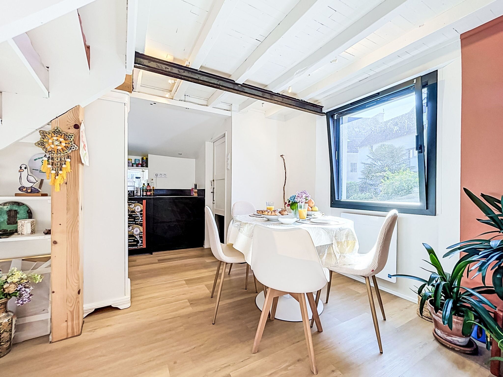 Comedor con una mesa lista para dos, vista de la cocina al fondo y un ventanal con vistas al exterior.