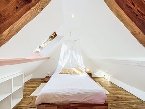 A bedroom with a sloped ceiling, a bed with a canopy, and a wooden floor. - Maison du Port by Interhome (Le Bono)