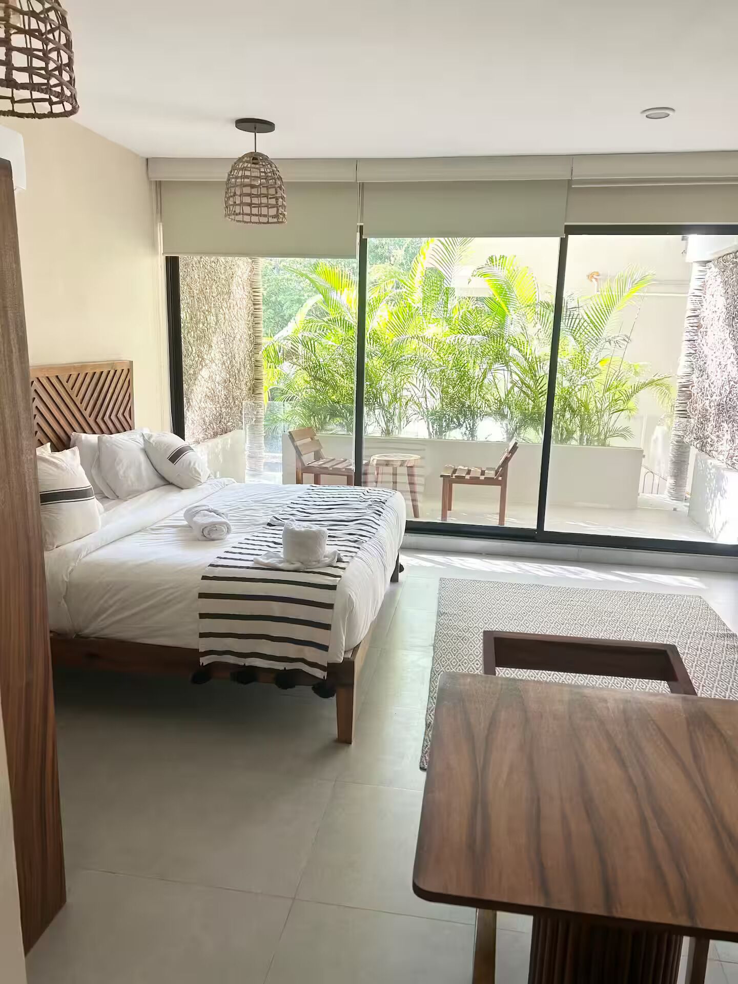 A hotel room with a bed, a small table, and a view of greenery outside.