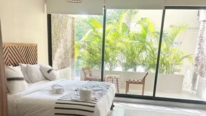 A hotel room with a bed, a table, and a view of greenery outside. - ModernBlair Vacation Rentals (Tulum)
