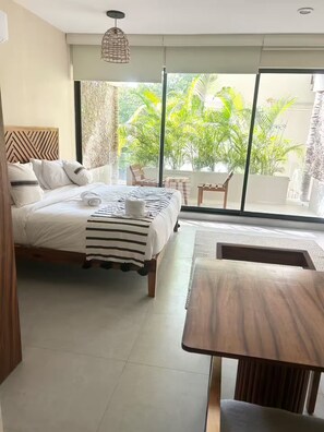 Ein Hotelzimmer mit Bett, Tisch und Blick auf Grünfläche.
