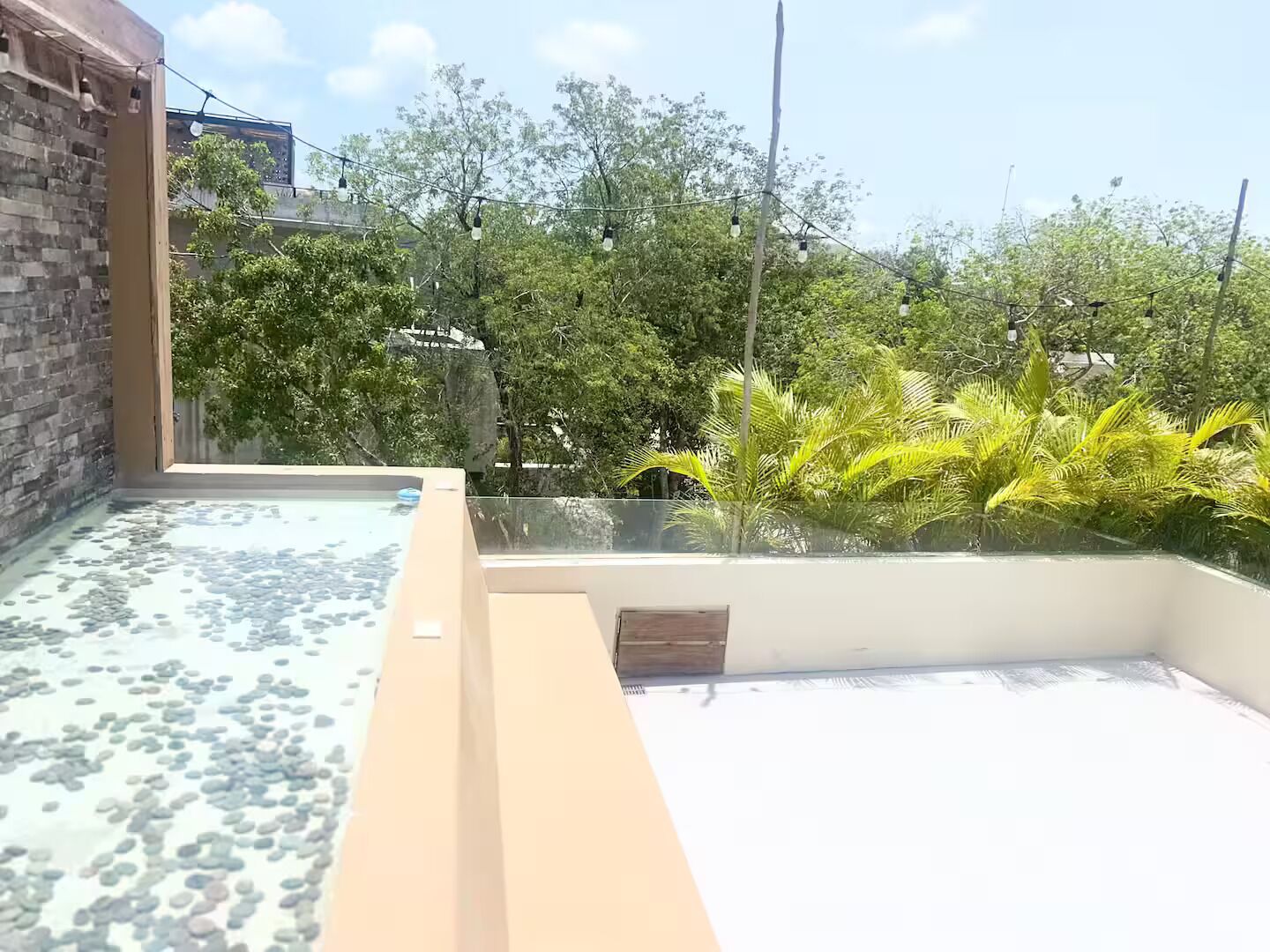 A rooftop terrace with a glass barrier, a pool with pebbles, and surrounding greenery.