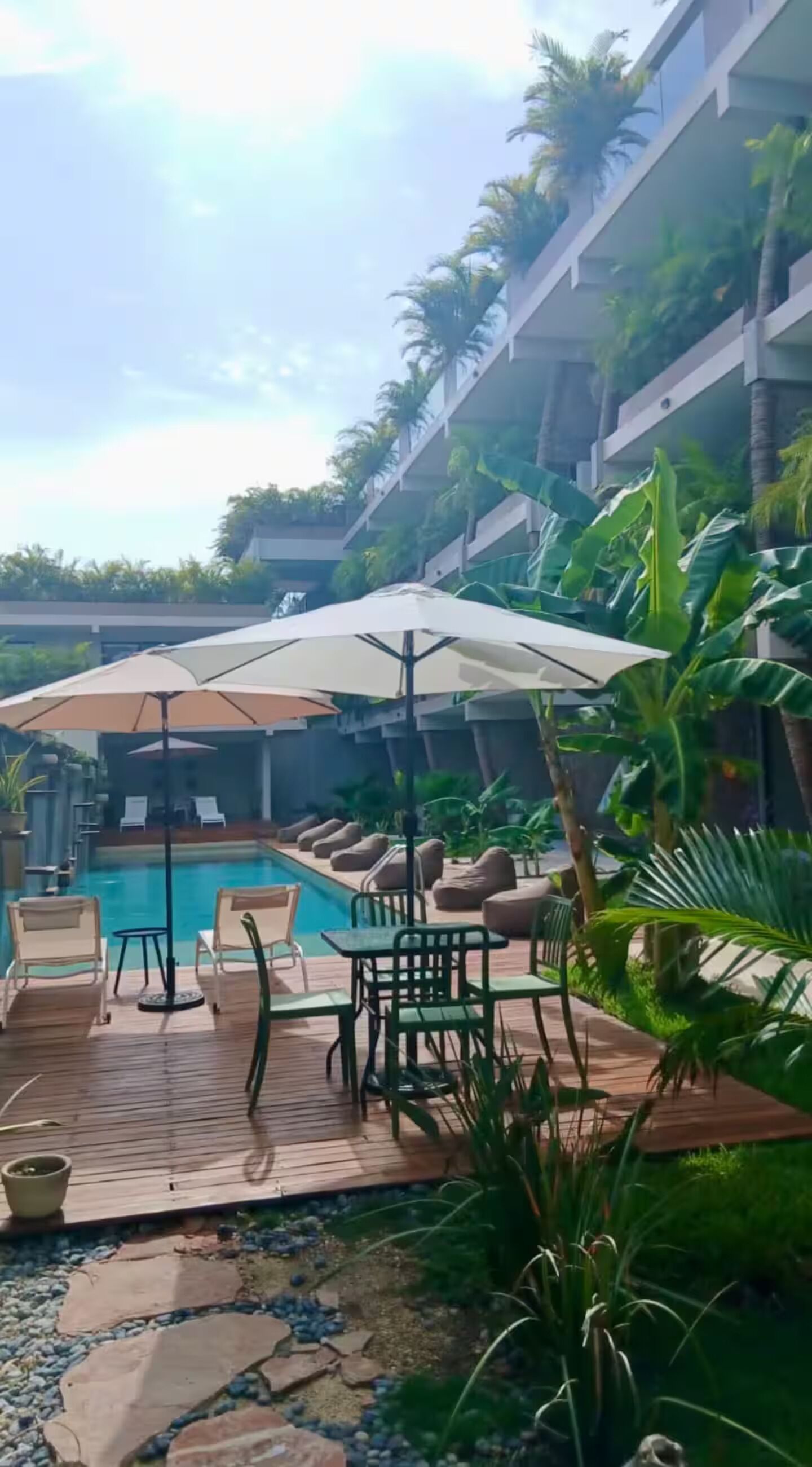 Un área junto a la piscina con sillones de descanso, sombrillas y una terraza de madera.