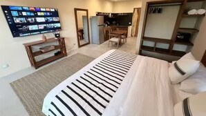 A hotel room with a bed, a desk, a television mounted on the wall, and a kitchenette area. - ModernBlair Vacation Rentals (Tulum)