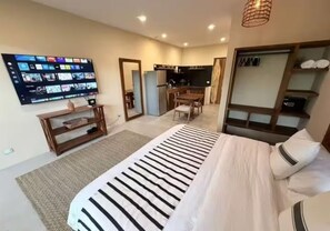 Ein Hotelzimmer mit Bett, Schreibtisch, Wand-Fernseher und einer Küchenzeile.