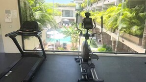 A gym with a treadmill and elliptical machine, large windows with a view of a pool and greenery. - ModernBlair Vacation Rentals (Tulum)
