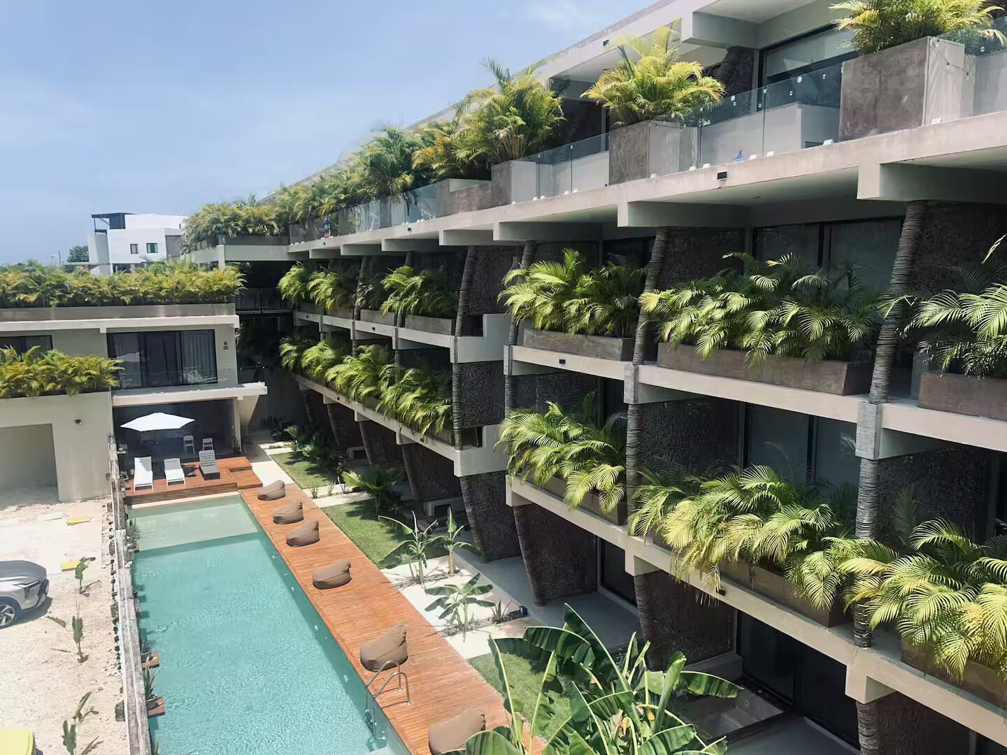 Een modern hotel met een dakterraszwembad, meerdere balkons met beplanting, en een heldere lucht.