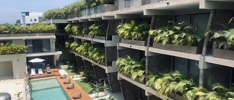 A modern hotel with a rooftop pool, multiple balconies with greenery, and a clear sky.