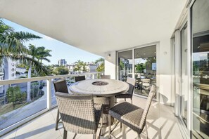 A balcony with a round table and wicker chairs, overlooking a cityscape with palm trees and buildings. - Chic Bay Harbor 3BR • Rooftop Pool • Free Parking (Bay Harbor Islands)