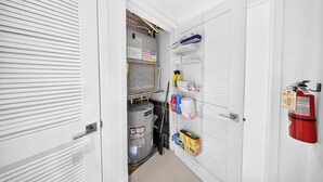 A narrow hallway with white doors, a fire extinguisher, and shelves with cleaning supplies. - Chic Bay Harbor 3BR • Rooftop Pool • Free Parking (Bay Harbor Islands)