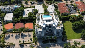 A multi-story hotel with a rooftop pool, surrounded by palm trees and adjacent to a parking lot. - Chic Bay Harbor 3BR • Rooftop Pool • Free Parking (Bay Harbor Islands)