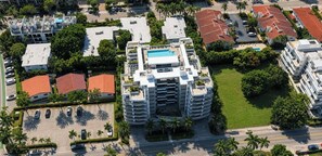 A multi-story hotel with a rooftop pool, surrounded by palm trees and adjacent to a parking lot.