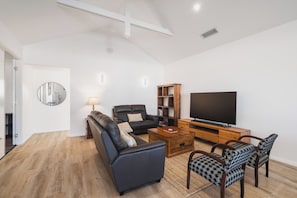 A modern living room with a sectional sofa, a coffee table, a TV, and a bookshelf. - Canal Living with a Private Jetty (Geographe)