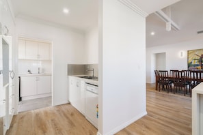 Uma cozinha moderna com armários brancos, lava-louças e um espaço de jantar com cadeiras de madeira e uma mesa.
