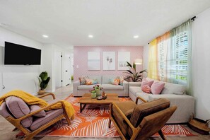 Uma sala de estar moderna com televisão de tela plana, um conjunto de sofá, uma mesa de centro e uma janela grande com cortinas.