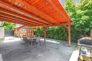 Eine überdachte Terrasse mit Esstisch und Stühlen, einem Grill und einer Holz-Pergola.