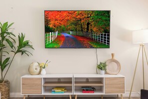 Una sala de estar moderna con un mueble blanco para equipo multimedia, un televisor de pantalla plana montado encima y una lámpara de pie a la derecha.