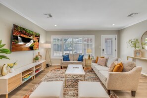 A living room with a sofa, coffee table, TV, and a large window with blinds. - Modern Monrovia Retreat By Old Town & City of Hope - Free Parking - Pet-Friendly (Monrovia)