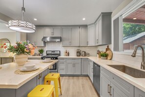 A modern kitchen with grey cabinets, a central island with stools, a stainless steel range hood, and a window with a view of greenery. - Modern Monrovia Retreat By Old Town & City of Hope - Free Parking - Pet-Friendly (Monrovia)