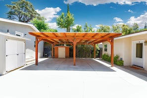 Un patio techado con una estructura de pérgola de madera, una puerta de garaje blanca y un cobertizo pequeño.
