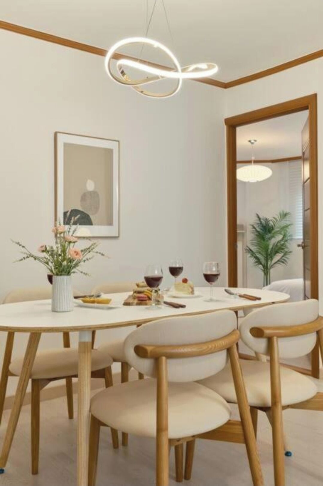 A dining area with a round table, six chairs, a vase with flowers, a framed picture on the wall, and a modern light fixture.