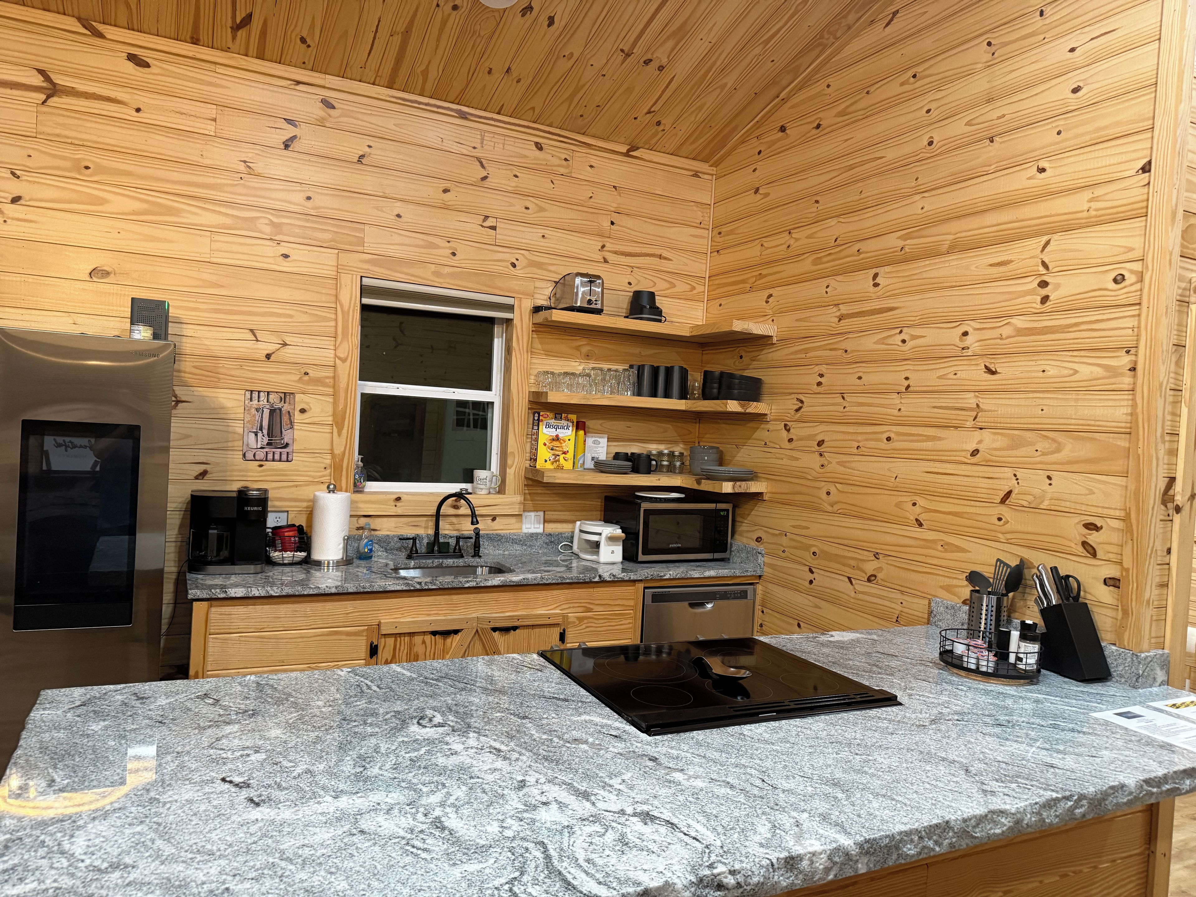 A compact kitchen with wooden walls, a stainless steel refrigerator, a microwave, a coffee maker, and a sink.