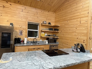 Eine kleine Küche mit Holzwänden, einem Edelstahlkühlschrank, einer Mikrowelle, einer Kaffeemaschine und einem Spülbecken.