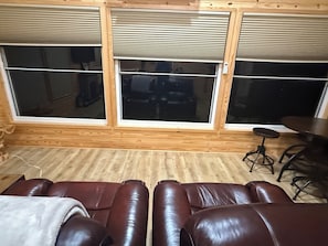 Ein Zimmer mit großem Fenster, einem braunen Ledersofa und einem kleinen Tisch mit Hocker.