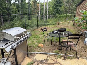 An outdoor patio with a gas grill, a round table, and two chairs.