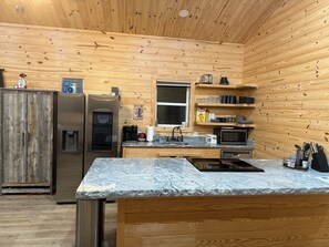 A compact kitchen with wooden walls, a stainless steel refrigerator, a microwave, and a coffee maker.