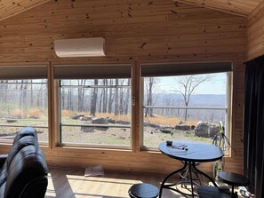 A cabin interior with a large window, a black leather sofa, a small round table, and a ceiling-mounted air conditioner.