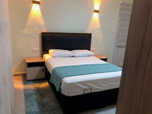 A neatly made bed with a dark headboard, two bedside tables, and a light-colored wall.