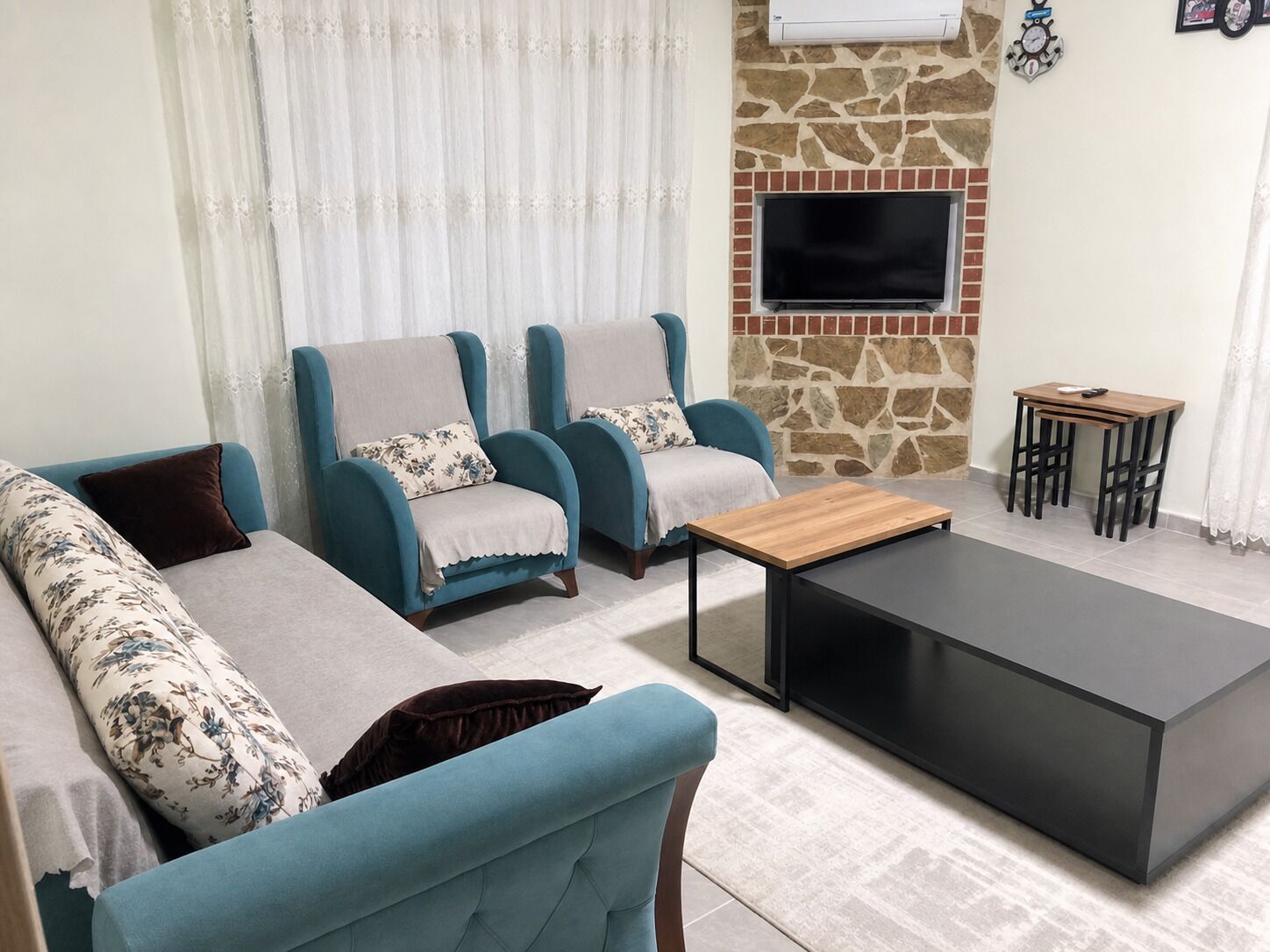 A living room with two armchairs, a sofa, a coffee table, and a TV mounted on a stone wall.