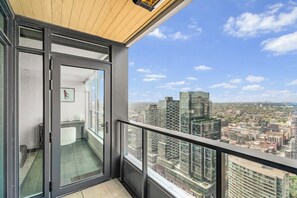 Uma varanda com porta de vidro que dá para um quarto, com vista para um horizonte urbano repleto de edifícios altos.