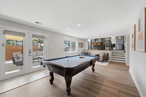 Ein modernes Wohnzimmer mit Billardtisch, einer Couch und einer Treppe, die in eine obere Etage führt.