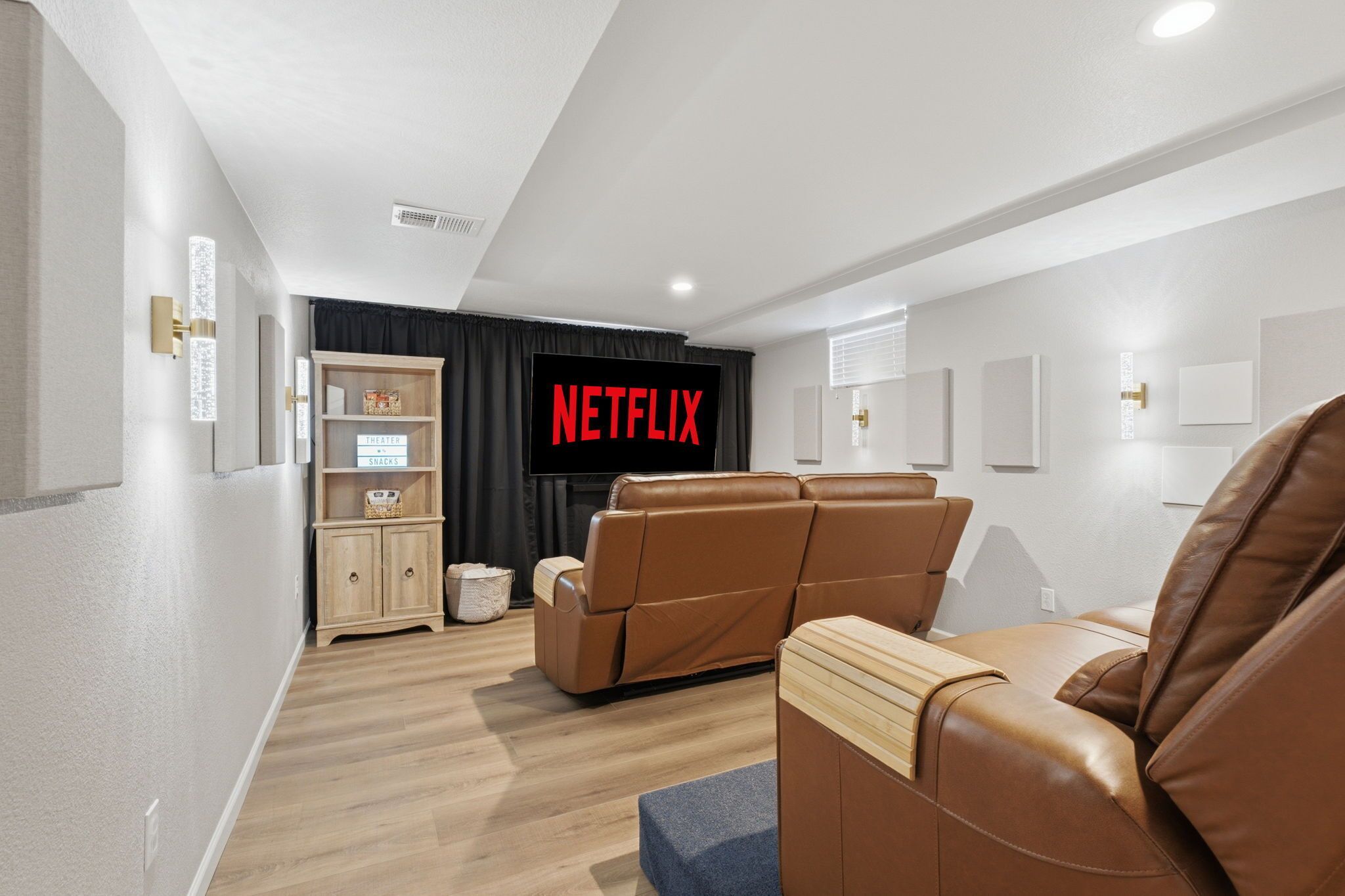 Una sala moderna con un televisor de pantalla plana, sillones reclinables de cuero, un mueble de madera y una estantería en la pared.