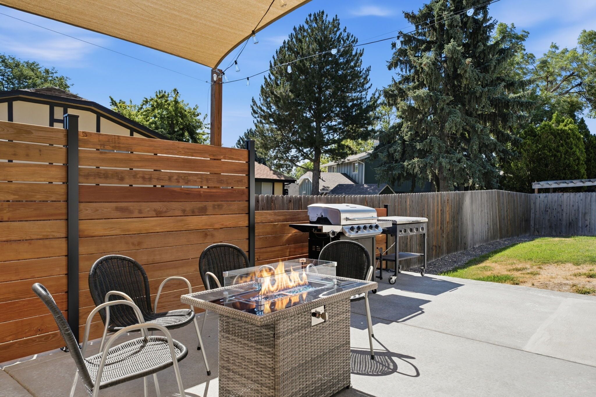 An outdoor patio with a fire feature, wicker furniture, and a grill.