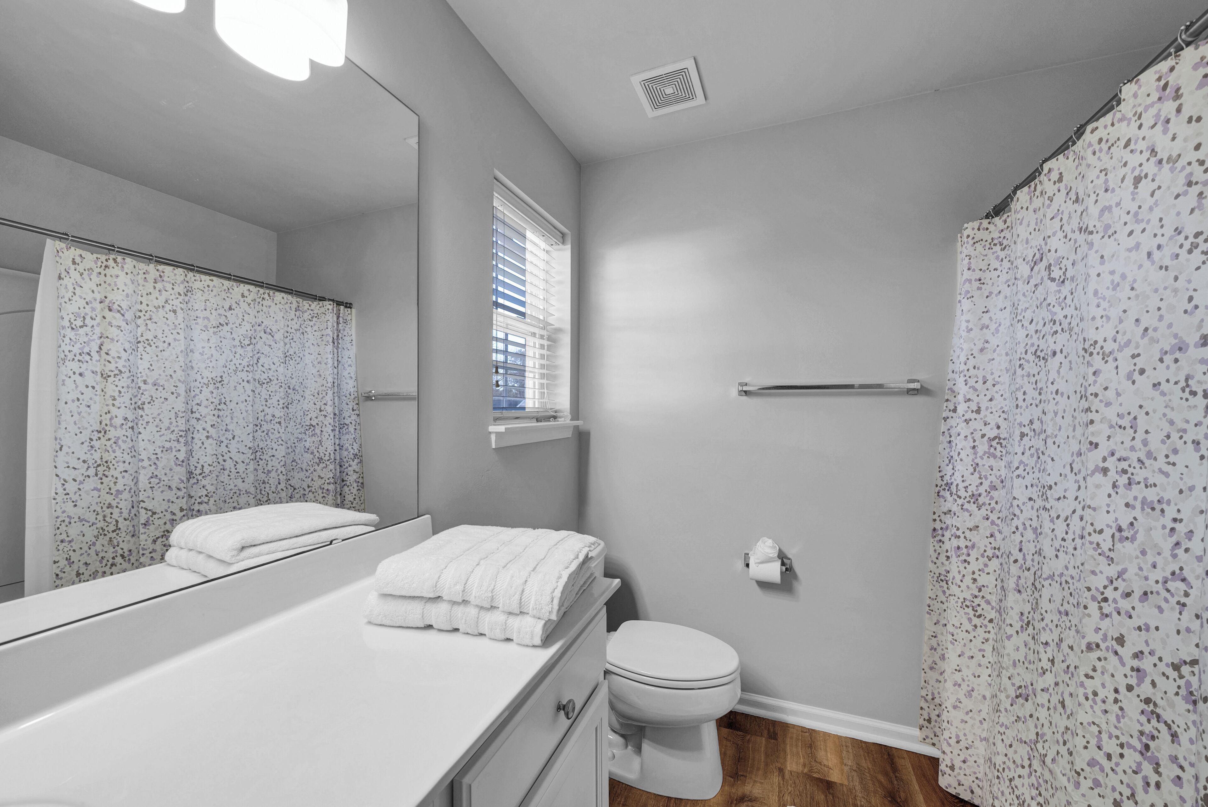 A bathroom with a white vanity, a toilet, a shower curtain, and a window with blinds.